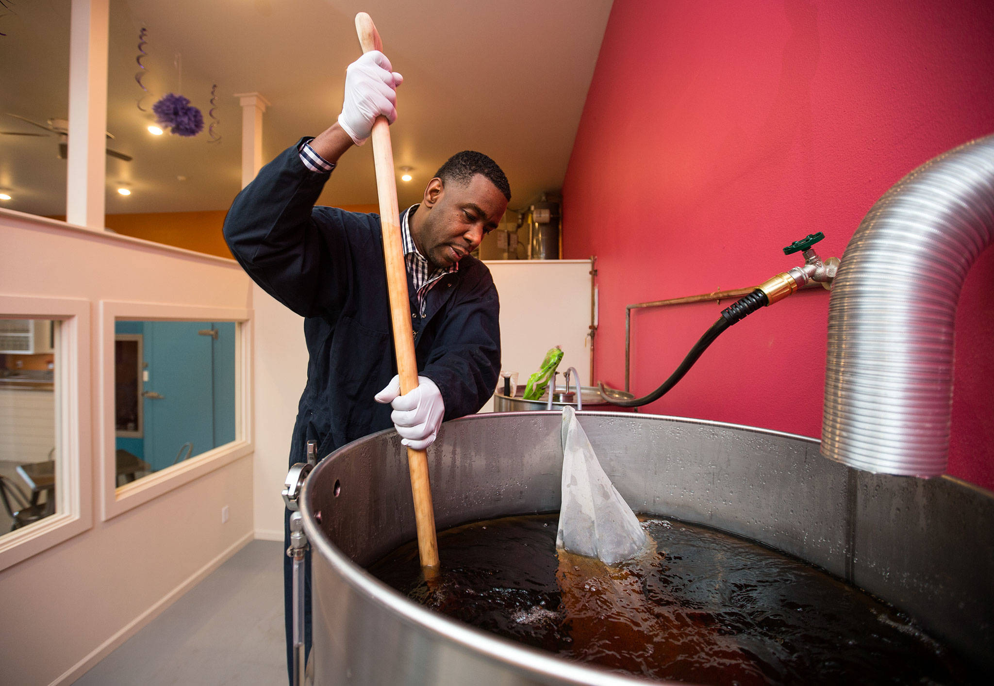 Lowell Profit, co-owner of the new GloryBucha kombucha bar in Arlington, stirs sugar in a vat of kombucha. The drink is a carbonated fermented tea. (Andy Bronson / The Herald)