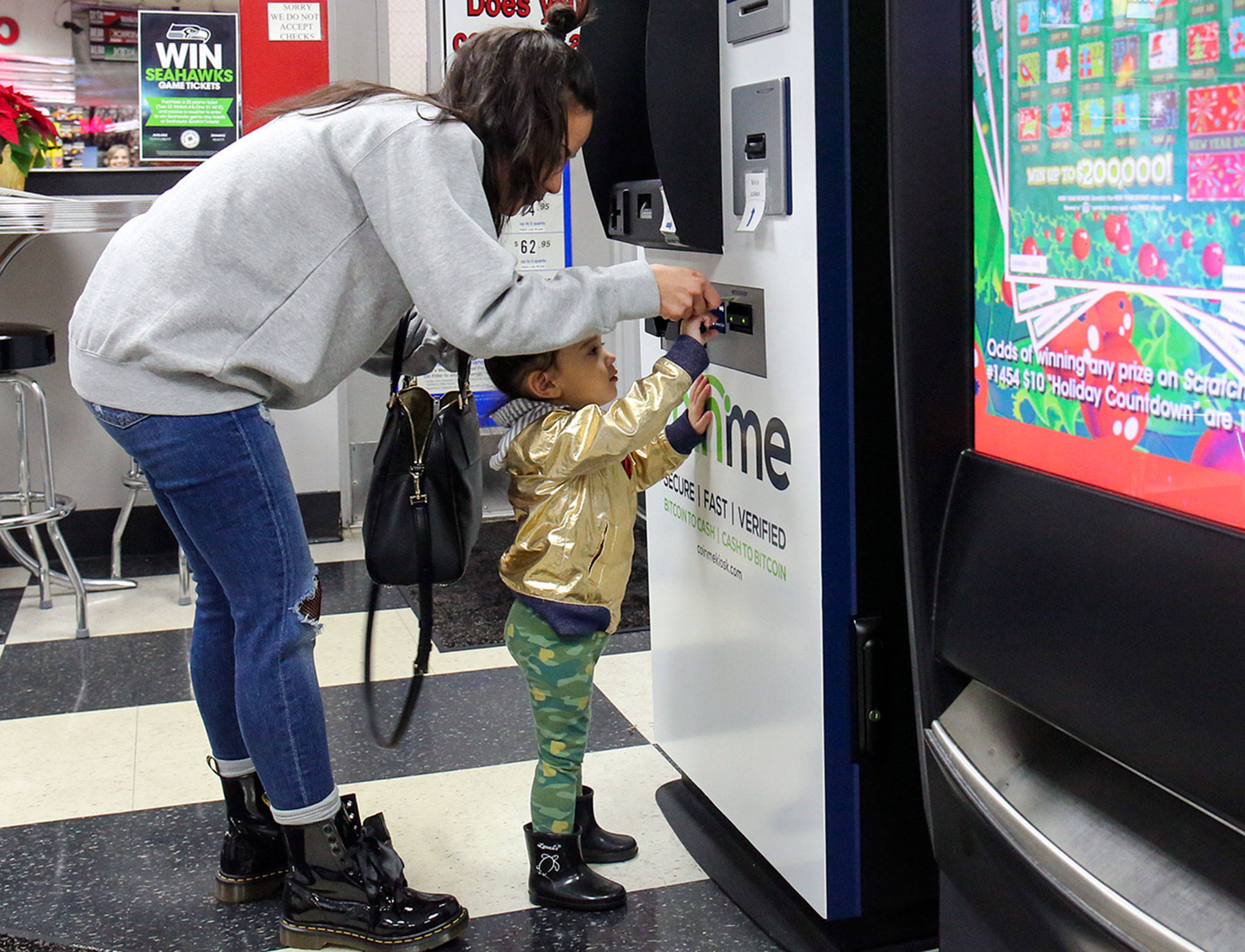 Karina Mia with Zoé Mia, 2, load funds into a bitcoin account through a Coinme machine at a mini-mart in Lynnwood. (Kevin Clark / The Daily Herald)