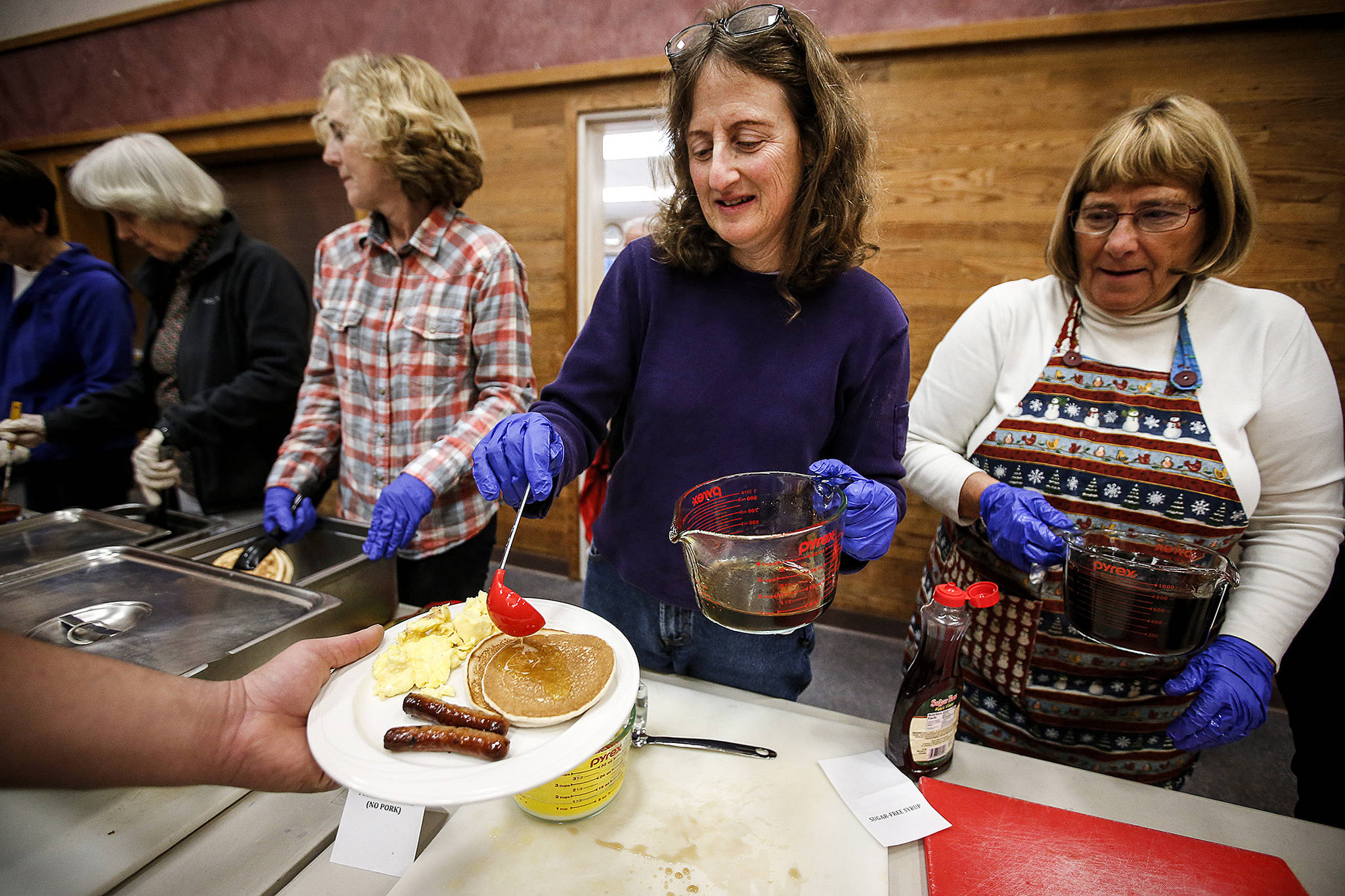 Barb Chessler (center) helps serve up breakfast along with other volunteers from Edmonds Unitarian Universalist Congregation at the Neighbors in Need breakfast at Trinity Lutheran in Lynnwood on Jan. 27. (Ian Terry / The Herald)