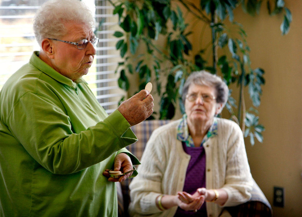 In July 2012, Sister Barbara Geib (left) of St. Mary of the Valley Catholic Church in Monroe delivers Communion to seniors and residents, including Alice Beach (back) at Regency Care Center in Monroe. At the time, Geib was celebrating her 60th year as a nun. (Dan Bates / The Herald)
