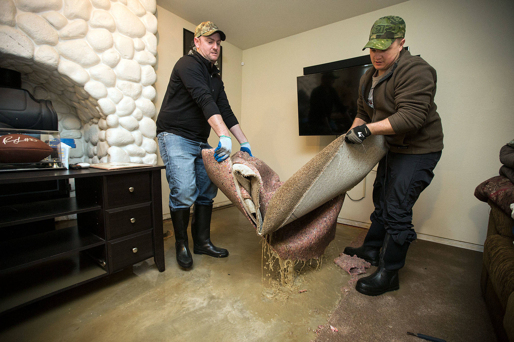 Homeowner James Edmondson (left) and his friend, Ryan Sund, carry out wet carpeting and padding from his flooded basement on Sexton Road on Monday in Snohomish. (Andy Bronson / The Herald)