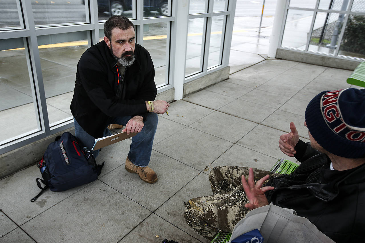 Volunteer Paul Olson (left), of Everett, completes a survey with a man at a bus stop on Smokey Point Boulevard during the annual point-in-time count of homeless people on Jan. 23. (Ian Terry / Herald file)