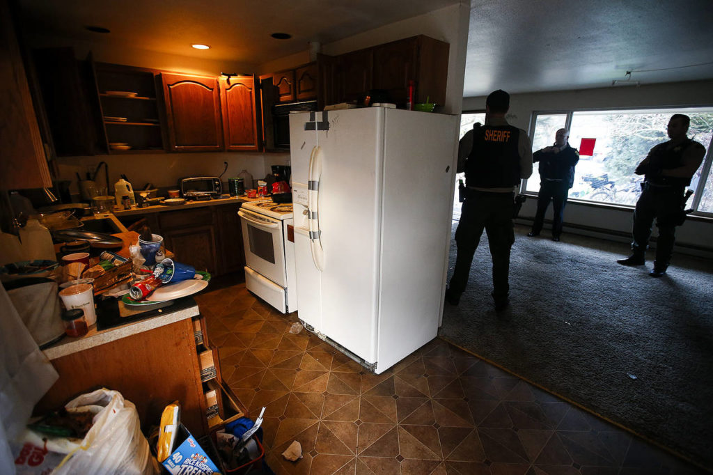 Snohomish County Sheriffճ deputies stand in the cleared-out living room of an Everett home used by squatters in in 2017. (Ian Terry / Herald file)
