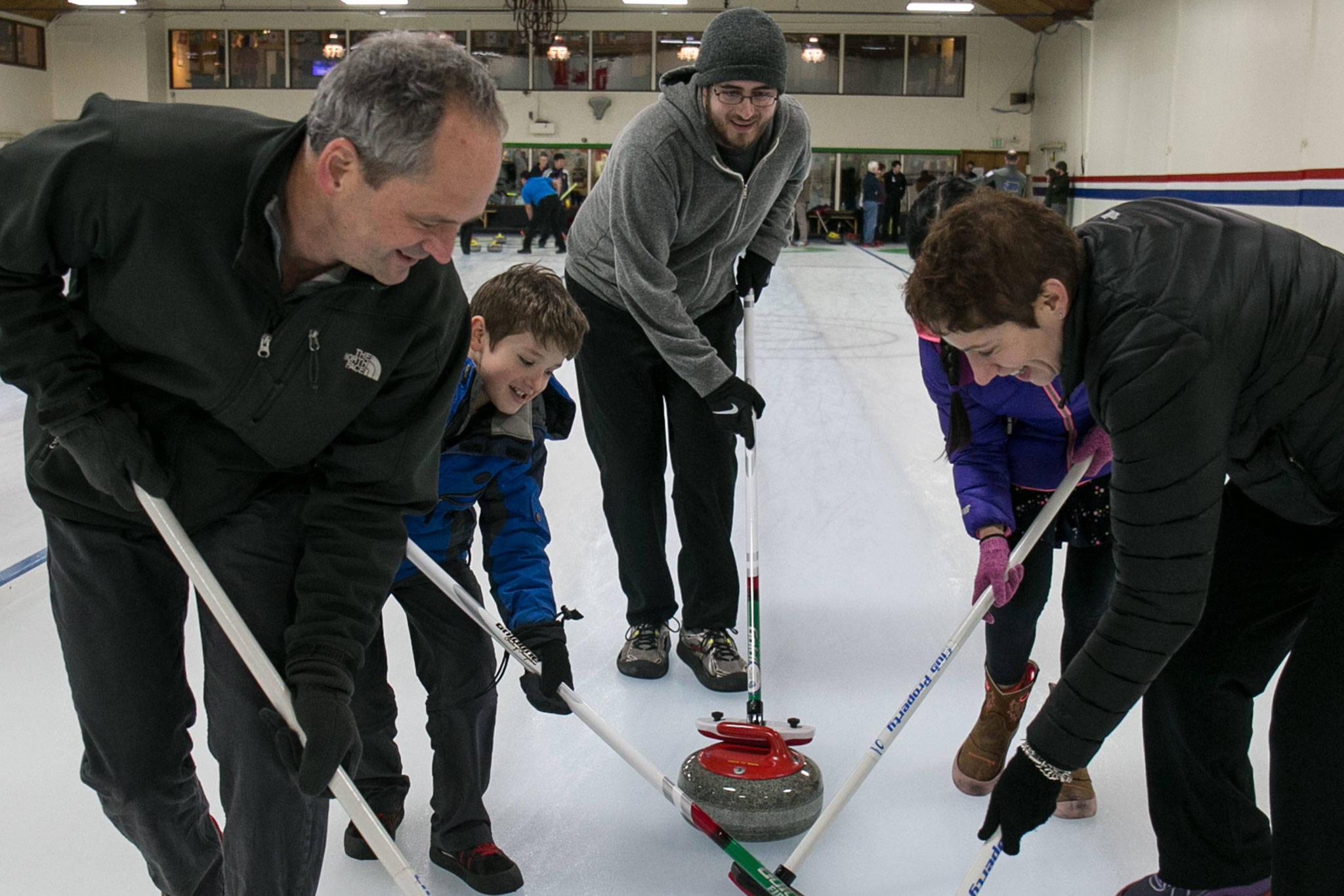 Bill Kerwin, (left to right) Lars Norman, Ruby Kerwin and Jelena Svircev sweep under the instruction on Zach Simon (center) during an open house at the Granite Curling Club in Seattle on Feb. 18. (Kevin Clark / The Daily Herald)