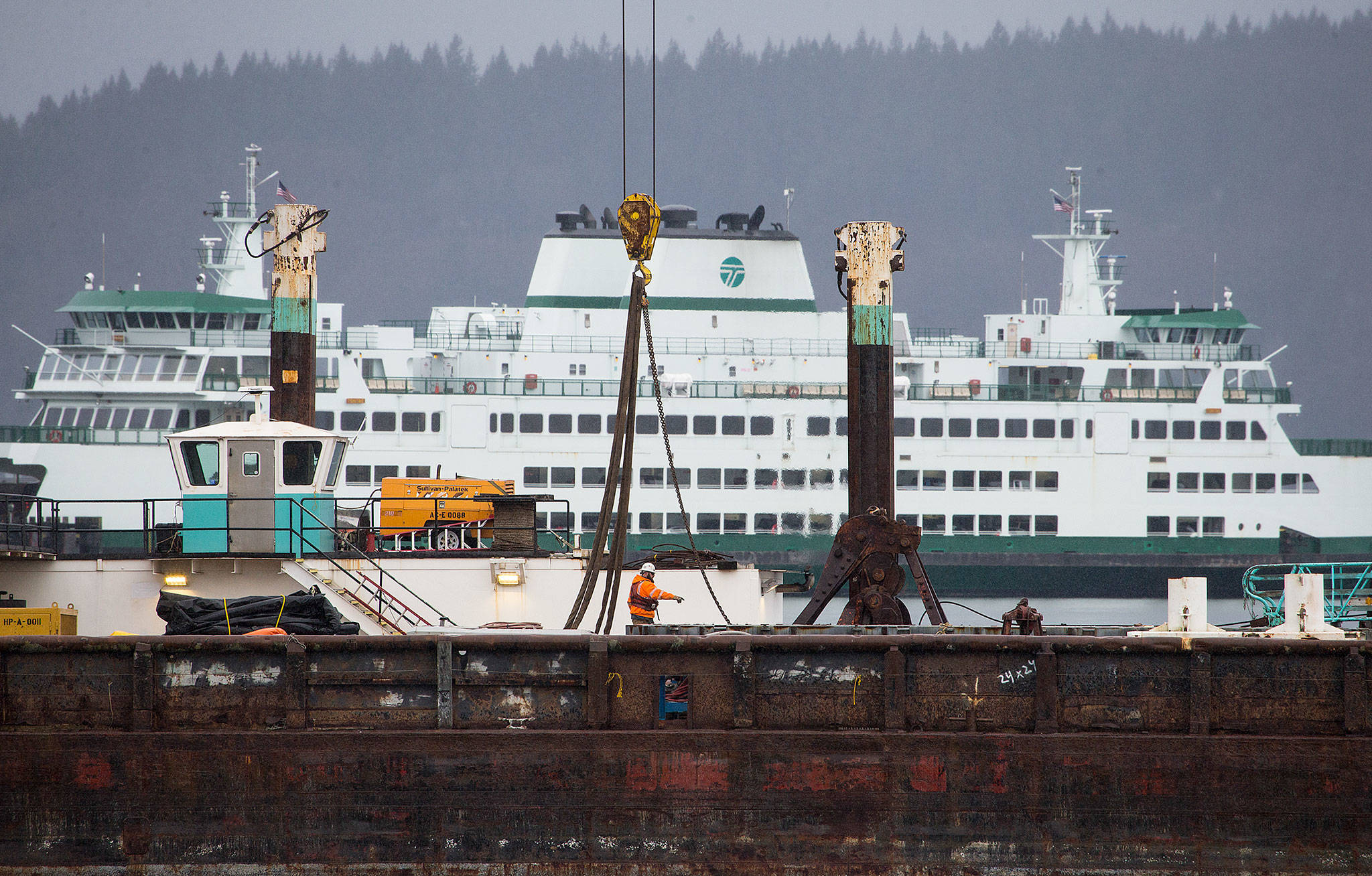 A worker directs others on a barge as construction continues Wednesday at the new Mukilteo ferry dock. The Legislature is proposing spending that would include $7.1 million to cover increased costs of constructing the new Washington State Ferry terminal in Mukilteo, plus $750,000 to provide greater use of solar panels than originally proposed. (Andy Bronson / The Herald)