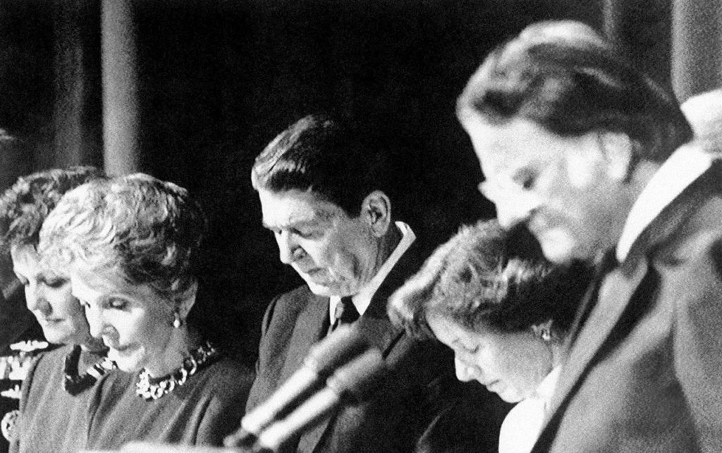 U.S. President Ronald Reagan, along with others, bow their heads and pray during the National Prayer Breakfast at a Washington hotelf on Feb. 5, 1987. From left are Transportation Secretary Elizabeth Dole, first lady Nancy Reagan, the President, Marcia Coats (wife of Rep. Daniel Coats of Indiana), and Rev. Billy Graham. During the breakfast, the president joined in a silent prayer for American hostages in Lebanon and missing church of England envoy Terry Waite. (AP Photo/J. Scott Applewhite)
