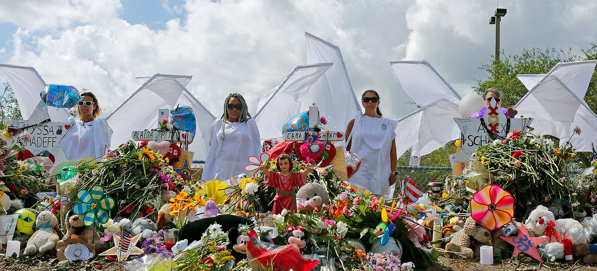 People dressed as angels stand by a makeshift memorial outside Marjory Stoneman Douglas High School in Parkland, Florida, on Sunday as thousands of students joined their parents in walking past the three-story building where the Feb. 14 shooting took place. (David Santiago/Miami Herald via AP)