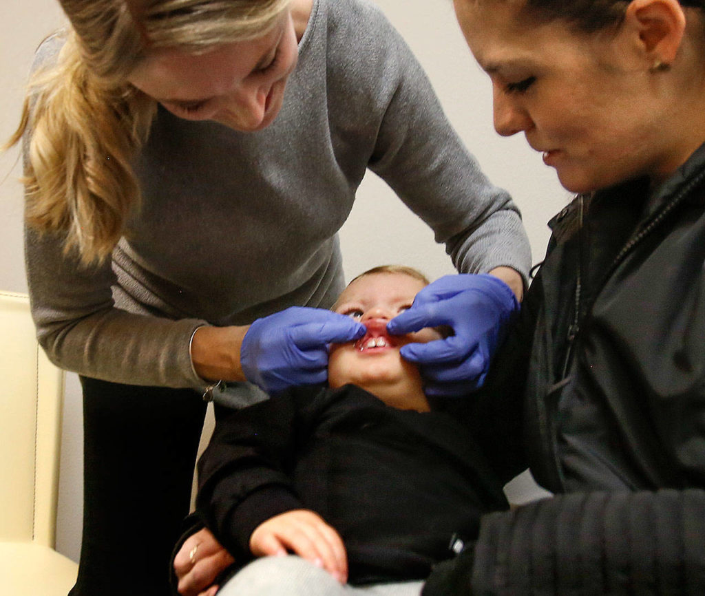 BreAnne Marcucci examines 1-year-old Braylon Machado’s front teeth while his mom, Gabbie Machado, holds him. (Dan Bates / The Herald)
