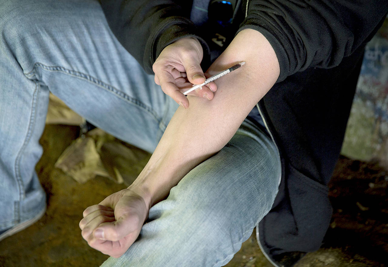 In this June 2017 photo, a man injects heroin into this arm under a bridge along the Wishkah River at Kurt Cobain Memorial Park in Aberdeen. (AP Photo/David Goldman, File)