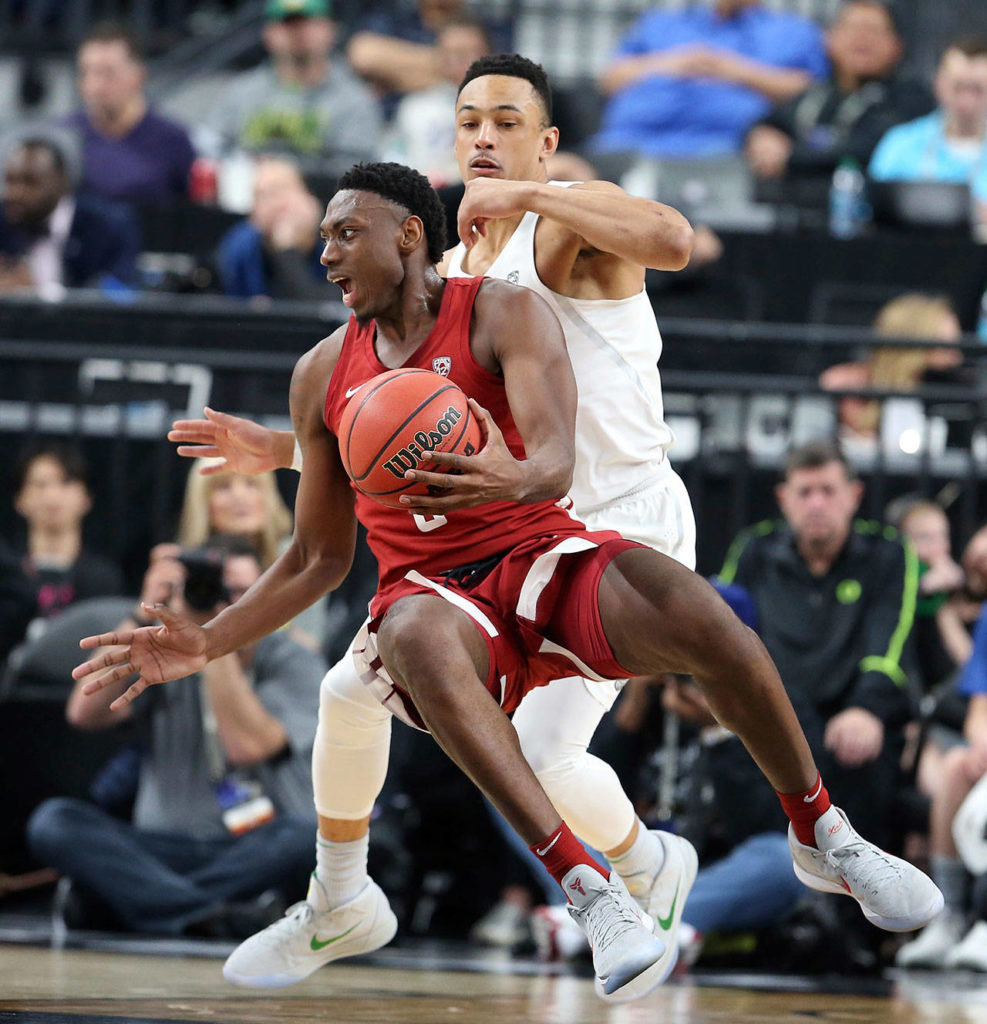 Washington State’s Robert Franks (front) tries to pass the ball as he falls to the court during Wednesday’s Pac-12 Tournament game in Las Vegas. Defending on the play is Oregon’s Elijah Brown. (AP Photo/Isaac Brekken)
