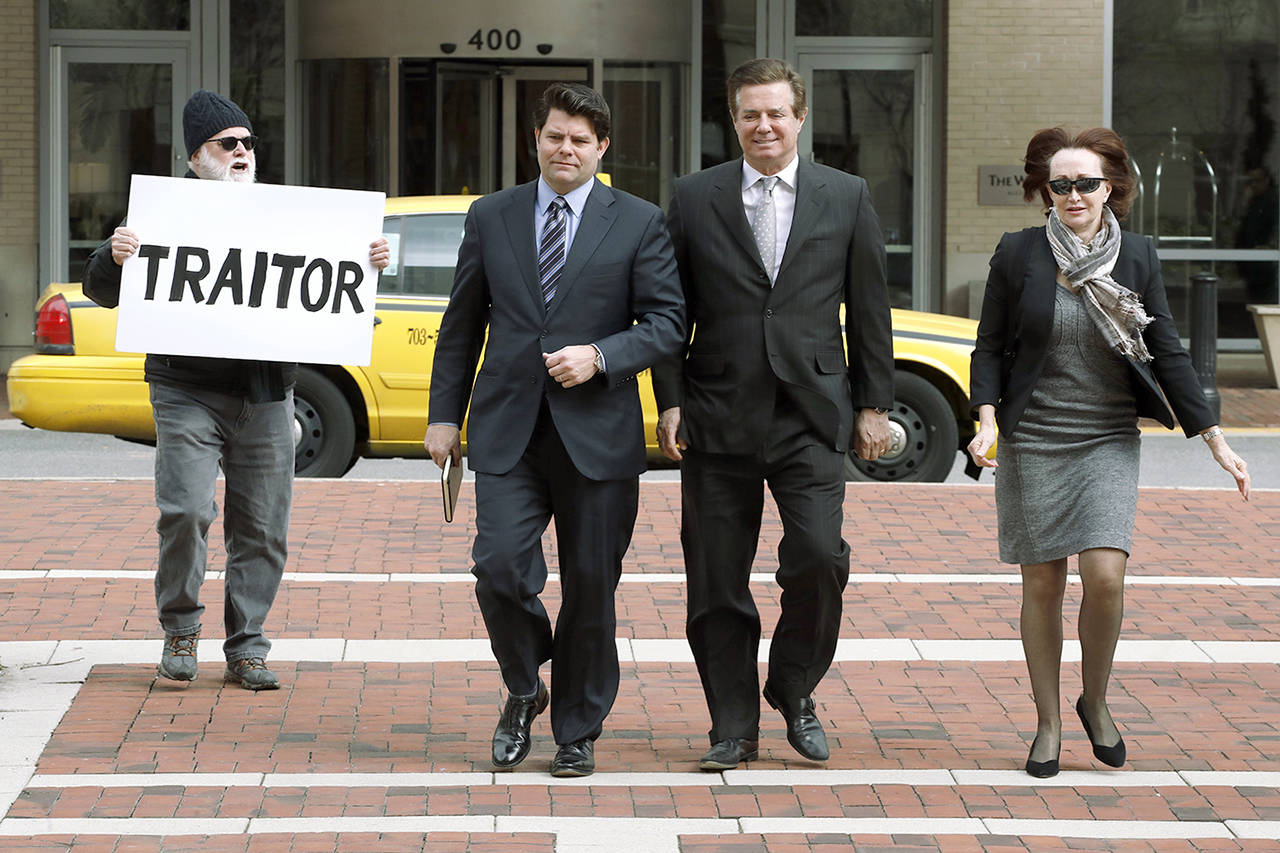 Paul Manafort (center right), President Donald Trump’s former campaign chairman, walks with this wife, Kathleen Manafort (right), and his spokesman Jason Maloni (left) as they arrive at the Alexandria Federal Courthouse for an arraignment hearing on his Eastern District of Virginia charges, in Alexandria, Virginia, on Thursday. Bill Christeson (left) holds up a sign. (AP Photo/Jacquelyn Martin)