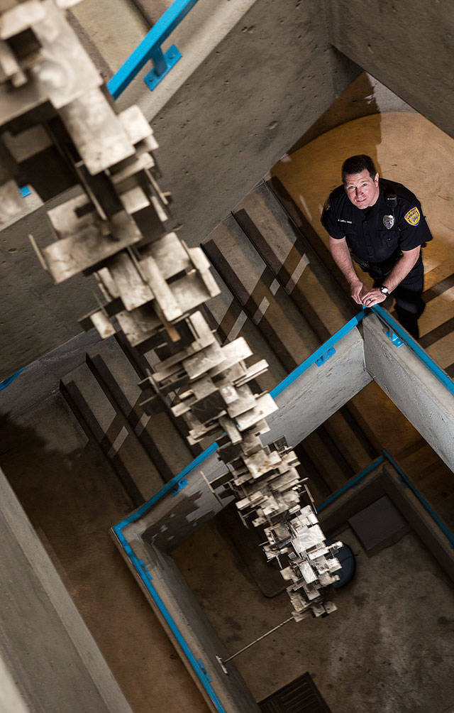 Everett Police Department’s Aaron Snell stands in a stairwell Friday where an art piece by artist Keith Imus hangs down its center. “It’s hiding in a stairwell now that nobody sees,” Imus says about his work. (Andy Bronson / The Herald)