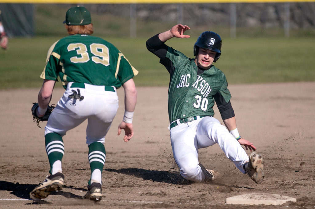 Jackson senior Carter Booth slides safely into third base past Marysville Getchell’s Gavyn Cookson during a game March 15, 2018, at Jackson High School in Mill Creek. (Kevin Clark / The Herald)

