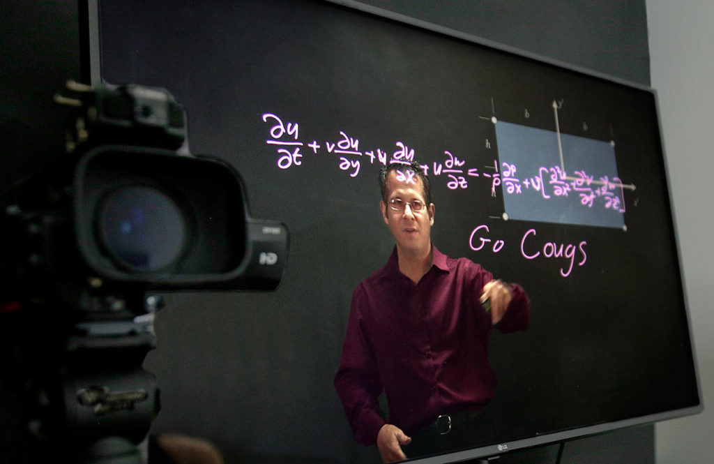 WSU Professor Gordon Taub can see everything his students can see on a big screen that is connected to a video camera at left. The imagery is flipped horizontally so you can read Go Cougs and decifer the math. (Dan Bates / The Herald)
