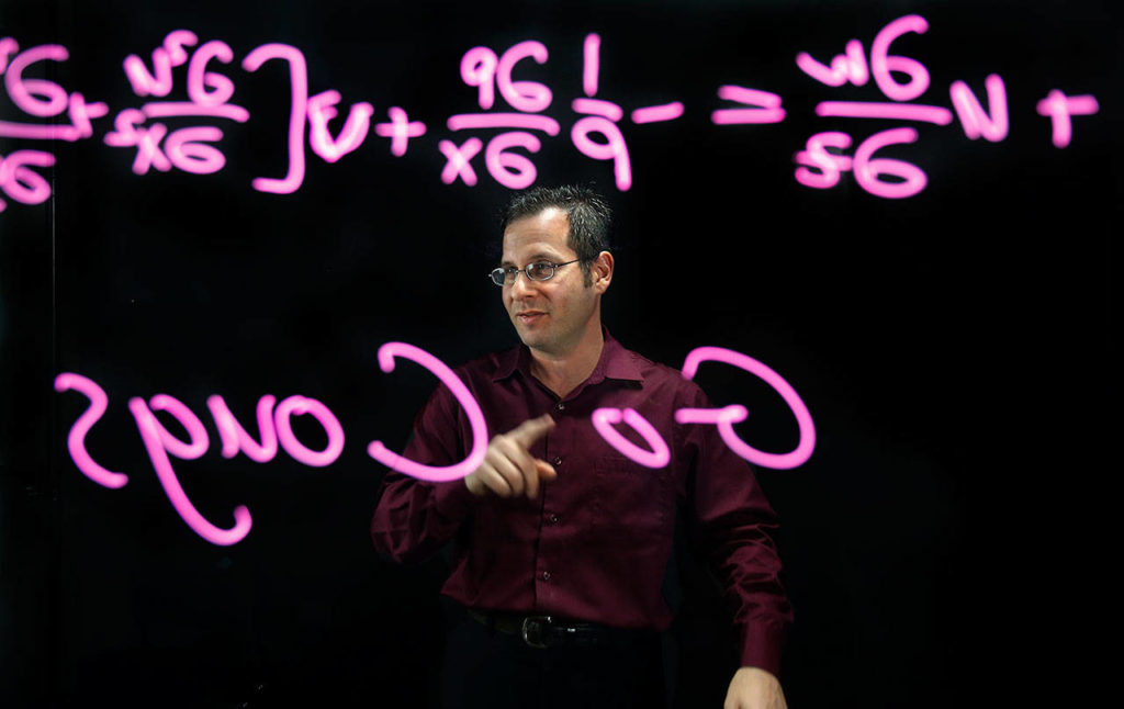 At WSU Everett, Professor Gordon Taub pre-records many of his lectures and publishes them on-line so his students can get into the subject matter and raise questions to him one-on-one if they need help. To accomplish this, he uses a &ldquo;lightboard studio&rdquo; which allows him to face the camera and write lessons or other messages on a large, thick glass surface. Stratigic lighting, and a black backgroung make the content stand out. A video camera records everything and the image is flipped horizontally so symbols and messages are not backwords. (Dan Bates / The Herald)
