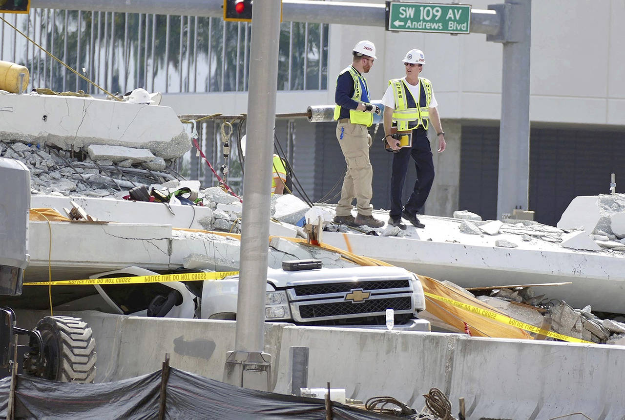 Inspectors walk over what remains of a pedestrian bridge near Florida International University on Sunday near Miami. (C.M. Guerrero/The Miami Herald via AP)