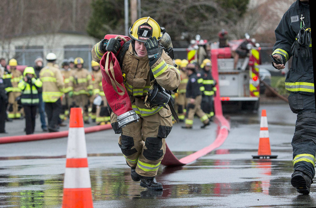 Marysville recruit Brian Donaldson holds onto his helmet as he drags a 5-inch line 200 feet in Snohomish County’s first fire training academy run through an obstacle course at the South County Snohomish Fire & Rescue training grounds on Monday in Everett. (Andy Bronson / The Herald)
