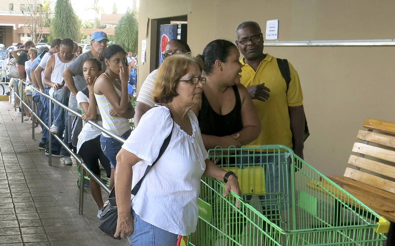 In this Sept. 25, 2017 photo, people wait in line outside a grocery store to buy food that wouldn’t spoil and that they could prepare without electricity, in San Juan. (AP Photo/Ben Fox, File)