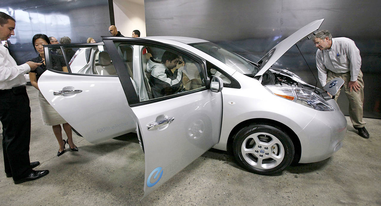 Employees and guests look over a new Nissan Leaf, an all-electric vehicle, after a ribbon-cutting ceremony for a new car dealership in Seattle in 2010. (AP Photo/Elaine Thompson, File)