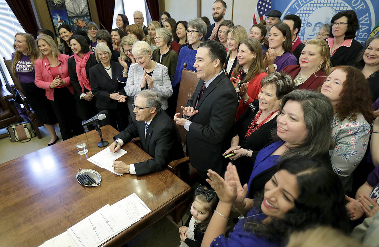 Washington Gov. Jay Inslee (seated) is applauded after he signed a measure at the Capitol in Olympia on Wednesday that requires Washington insurers offering maternity care to also cover elective abortions and contraception. (AP Photo/Ted S. Warren)