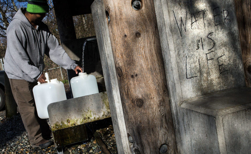 Water is Life is spray painted on a support as Faisal Warsame fills up several water containers at the artesian well on 164th Street on April 2 in Lynnwood. The well, also known as Well No. 5 or the 164th Street Artesian Well, is in excess of 400 feet in depth and is cased to approximately 120 feet. The well flows at a rate of about 10 gallons per minute. (Andy Bronson / The Herald)
