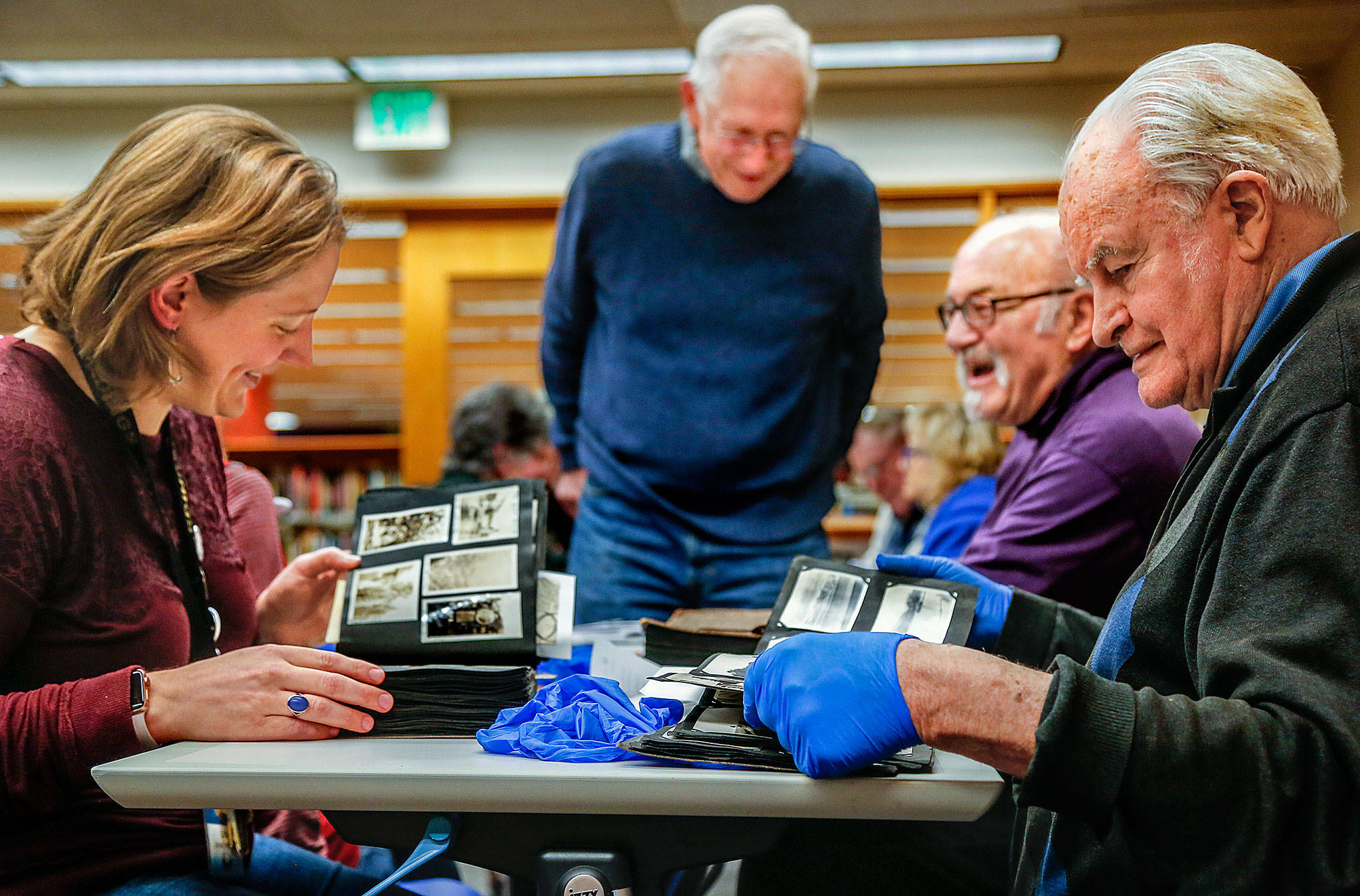 From left, library historian Lisa Labovitch, Jerry Solie (standing), and history buffs Dave Ramstad and William Vincent (right) enjoy one another’s light conversation while studying images in dozens of scrapbooks and photo albums Tuesday night at the Everett Public Library. (Dan Bates / The Herald)