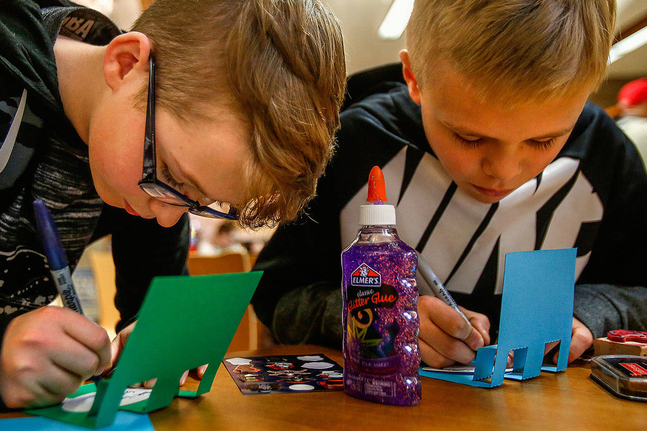 Carter Howell, 12, (left) from Post Middle School, and Bjorn Gudgeon, 12, from Haller Middle School print messages on pop-up cards they made during a card-making party at Arlington Library April 12. The cards were to be sent to the nonprofit Cards for Hospitalized Kids. (Dan Bates / The Herald)