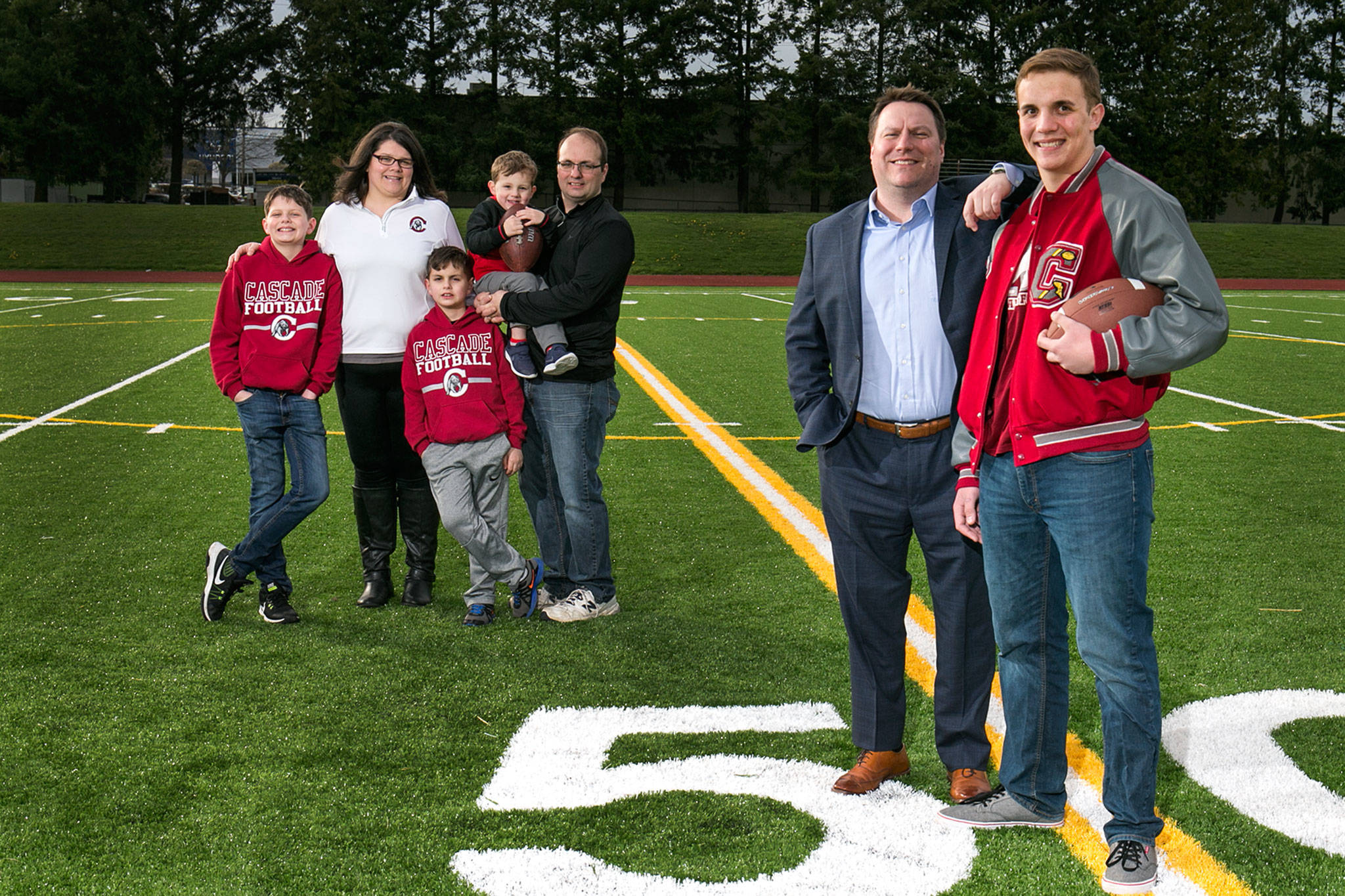 Cascade junior Chris Rabideau (far right) stands with his Big Brother Clint Diehm and his adopted family (from left to right) Ethan Rabideau, Leslie Rabideau, Zachery Rabideau, Isaiah Rabideau and Jeremy Rabideau on the football field at Cascade High School in Everett on April 2, 2018. Chris is a two-way standout lineman on the Bruins football team. (Kevin Clark / The Herald)
