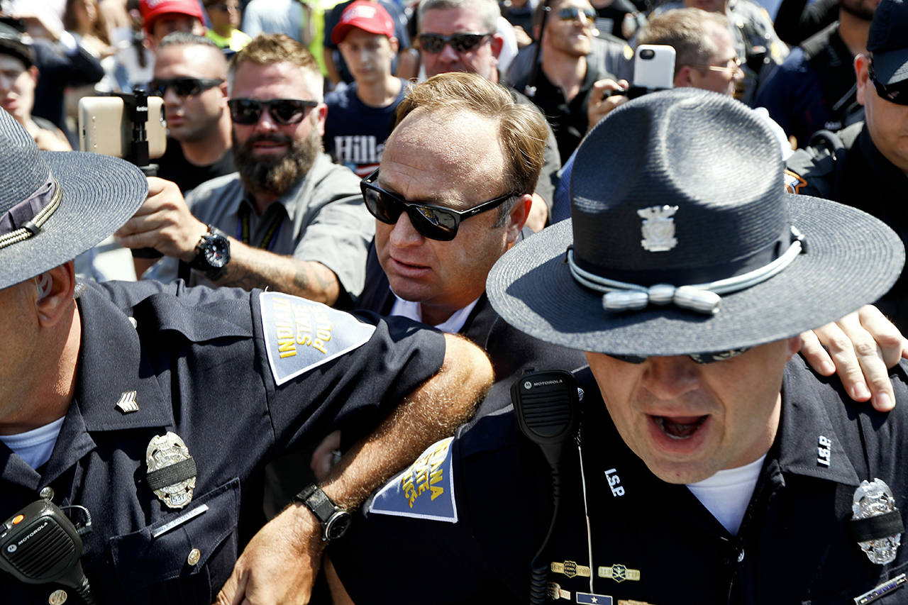 Alex Jones (center), an American conspiracy theorist and radio show host, is escorted out of a crowd of protesters after he said he was attacked in Public Square in 2016, in Cleveland, during the second day of the Republican convention. (AP Photo/John Minchillo, file)