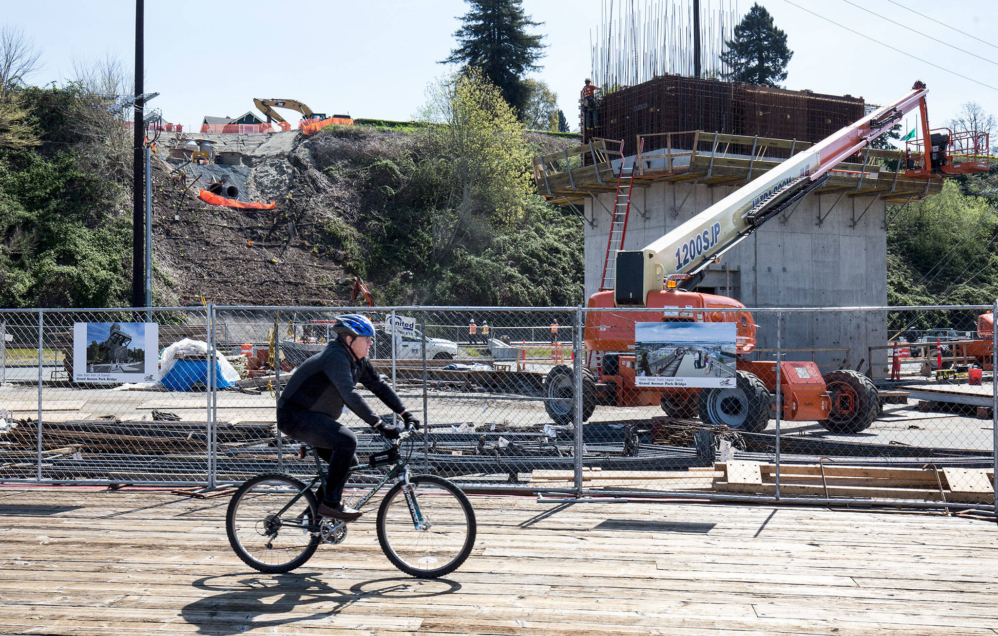 A bicyclist passes workers preparing rebar for a pedestrian bridge that will connect Grand Avenue Park with the Everett waterfront. (Andy Bronson / The Herald)