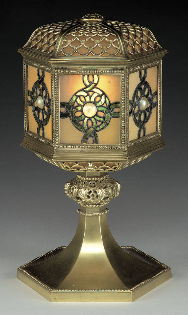 This 15½-inch-tall table lantern marked “Tiffany Studios New York” sold for $6,655 at a recent James D. Julia auction in Maine. It has a shade with glass panels centered with a cabochon jewel. The stem is decorated bronze with a gold patina. (Cowles Syndicate Inc.)
