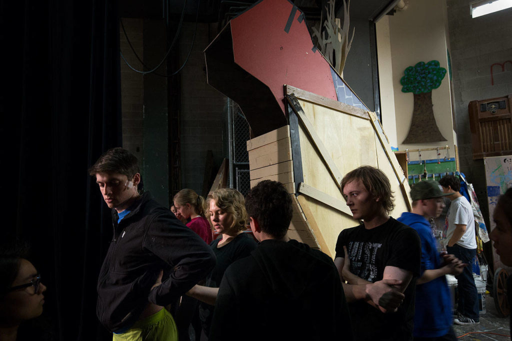 A giant wooden rabbit dominates over stage manager Laura Schmitt, center, as she adjusts a battery pack on the back of Mitchell Beard backstage during a rehearsal of “Spamalot” at Kamiak High School. (Andy Bronson / The Herald)
