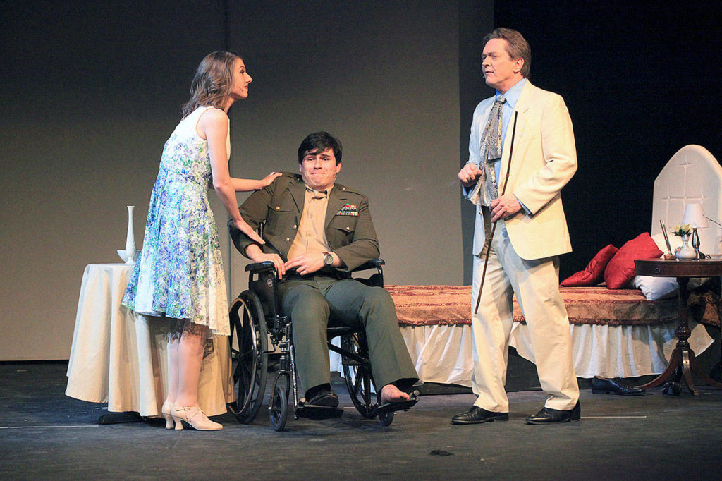 Christine (Andee Albert) is getting conned by Freddy (Gabriel Ponce), who is posing as a paralyzed veteran (in the wheelchair), and Lawrence (Jay Vilhauer), who is posing as a doctor who claims he can get Freddy to walk again. (Edmonds Driftwood Players)
