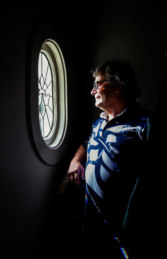 Stepping inside a closet in an upper-floor apartment, builder Gary Nelson is bathed in light from a small, leaded oval window. (Dan Bates / The Herald)
