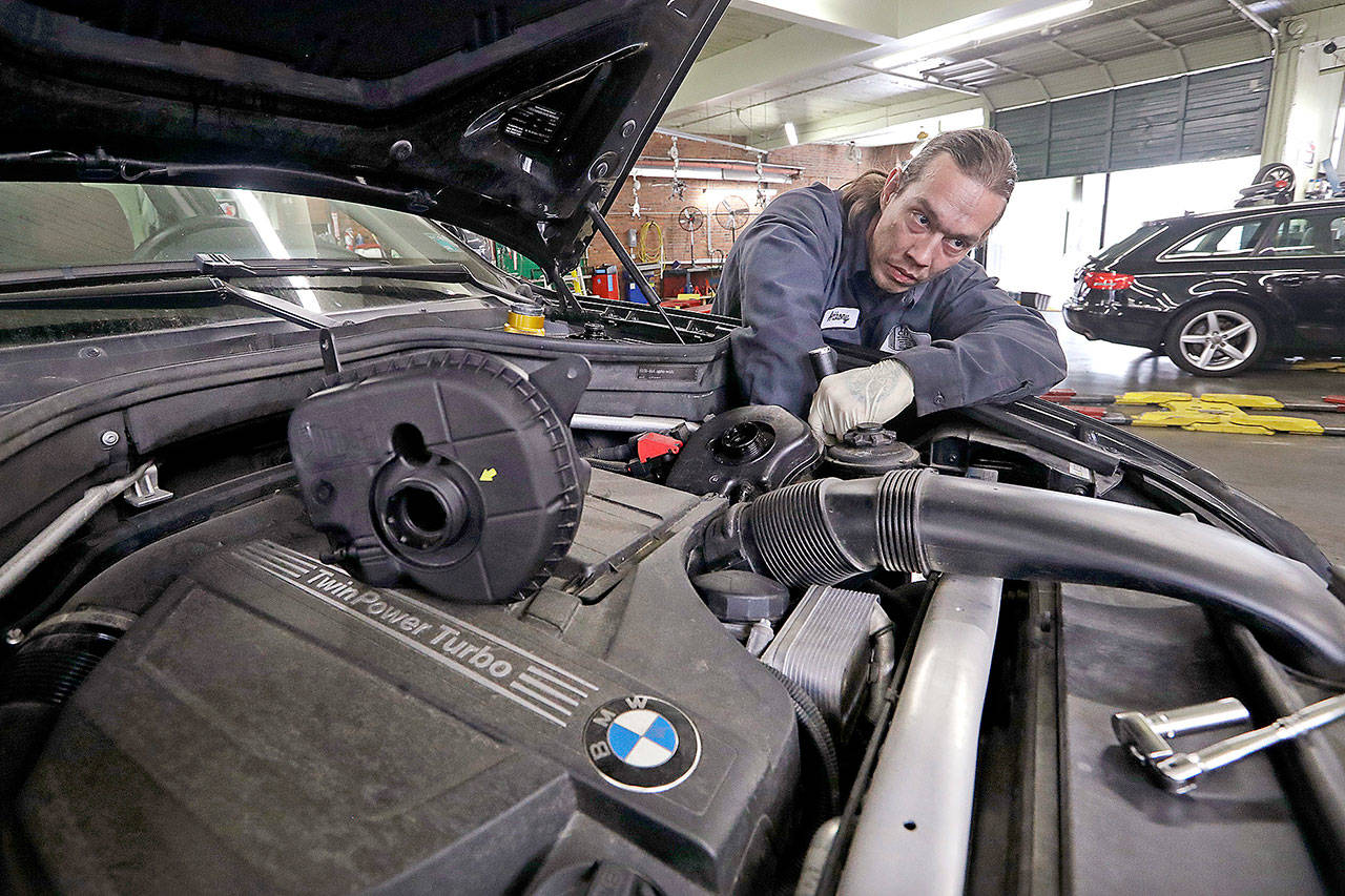 In this Wednesday, April 25, 2018, photo, auto technician Anthony Sterns works to replace the coolant expansion tank on a 2011 BMW at the Fat City German Car service shop in Seattle. At first, dumping your old car might seem like a no-brainer, and you can’t help picturing how good you would look in that new car. But automotive experts say you’ll almost always come out ahead, at least financially, by fixing old faithful. (AP Photo/Elaine Thompson)