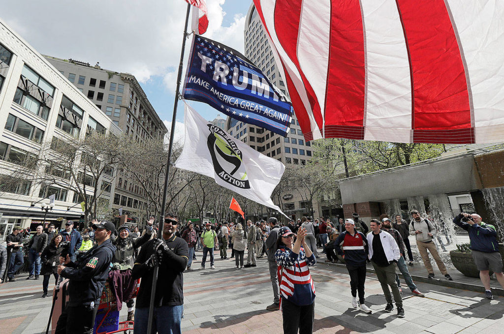 A man who declined to give his game holds a flag pole that includes a flag promoting President Donald Trump as he attends a May Day rally held by the Patriot Prayer group Tuesday in Seattle. (AP Photo/Ted S. Warren)
