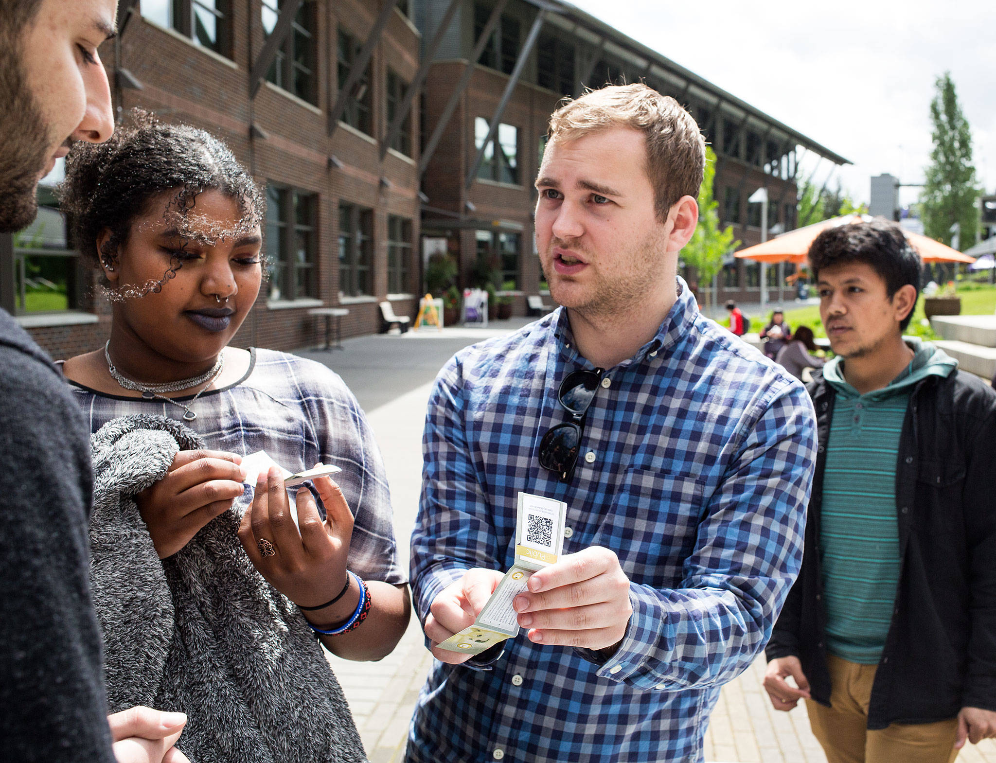 Cryptocurrency and Blockchain Club president Zach Nelson explains to a pair of students how the currency works while handing out free cryptocurrency at the University of Washington Bothell on Wednesday, May 9, 2018 in Everett, Wa. (Andy Bronson / The Herald)