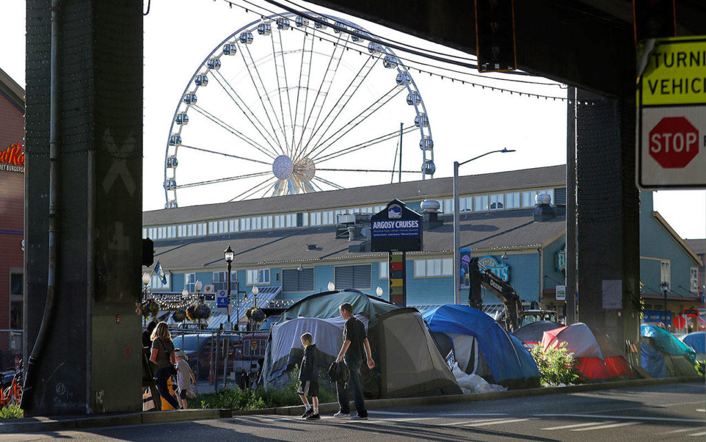 With the Seattle Great Wheel in the background, pedestrians walk past tents set up along a sidewalk at the Seattle waterfront Monday. Seattle’s latest tax proposal to combat homelessness takes aim at large businesses such as Amazon that have helped drive the city’s economic boom. But businesses and others say the so-called head tax is misguided and potentially harmful and they question whether the city is effectively using the tens of millions of dollars it already spends on homelessness each year. (AP Photo/Ted S. Warren)
