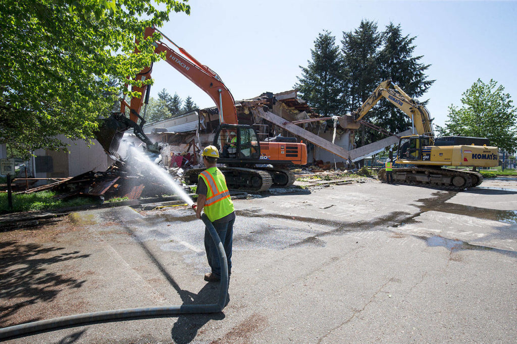 James Pearson hoses down roofing material pulled down while another excavator moves one of the ceiling beams as North Hill Resouces crews demolish the Hal Moe Pool on Monday in Snohomish. (Andy Bronson / The Herald)
