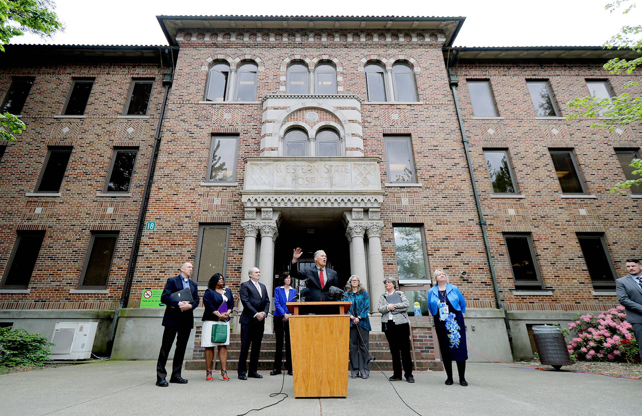 Washington Gov. Jay Inslee (center) speaks Friday in front of Western State Hospital in Lakewood, where he outlined a five-year plan for the state’s mental health system. (AP Photo/Ted S. Warren)