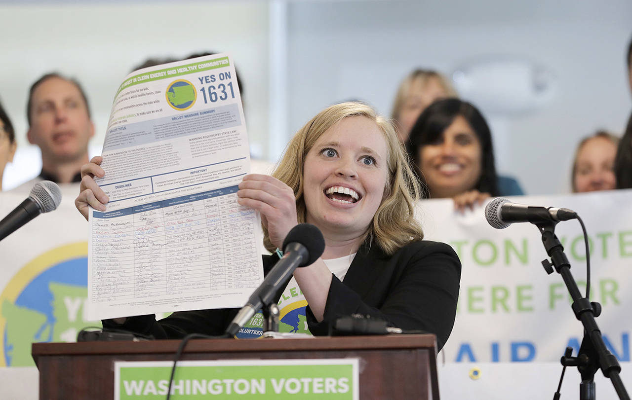 Abigail Doerr, campaign director for Yes on 1631, holds up an initiative petition with signatures on it at a May 10 rally to kick off the campaign for “Yes on 1631,” a coalition in favor of Initiative 1631, which would levee a fee on carbon and other greenhouse-gas emissions in Washington. (AP Photo/Ted S. Warren)