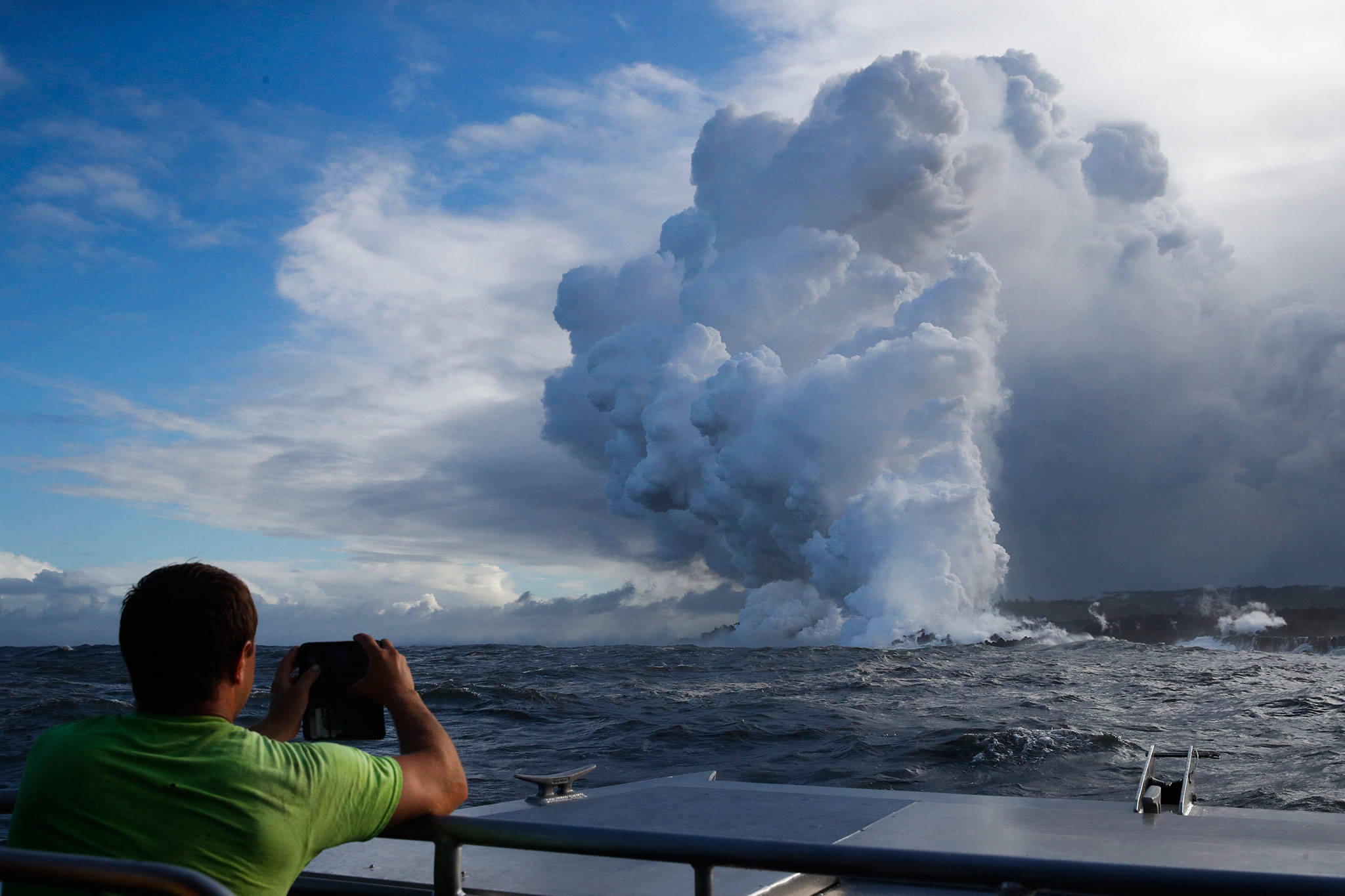 Joe Kekedi takes pictures as lava enters the ocean, generating plumes of steam near Pahoa, Hawaii on May 20. (AP Photo/Jae C. Hong)