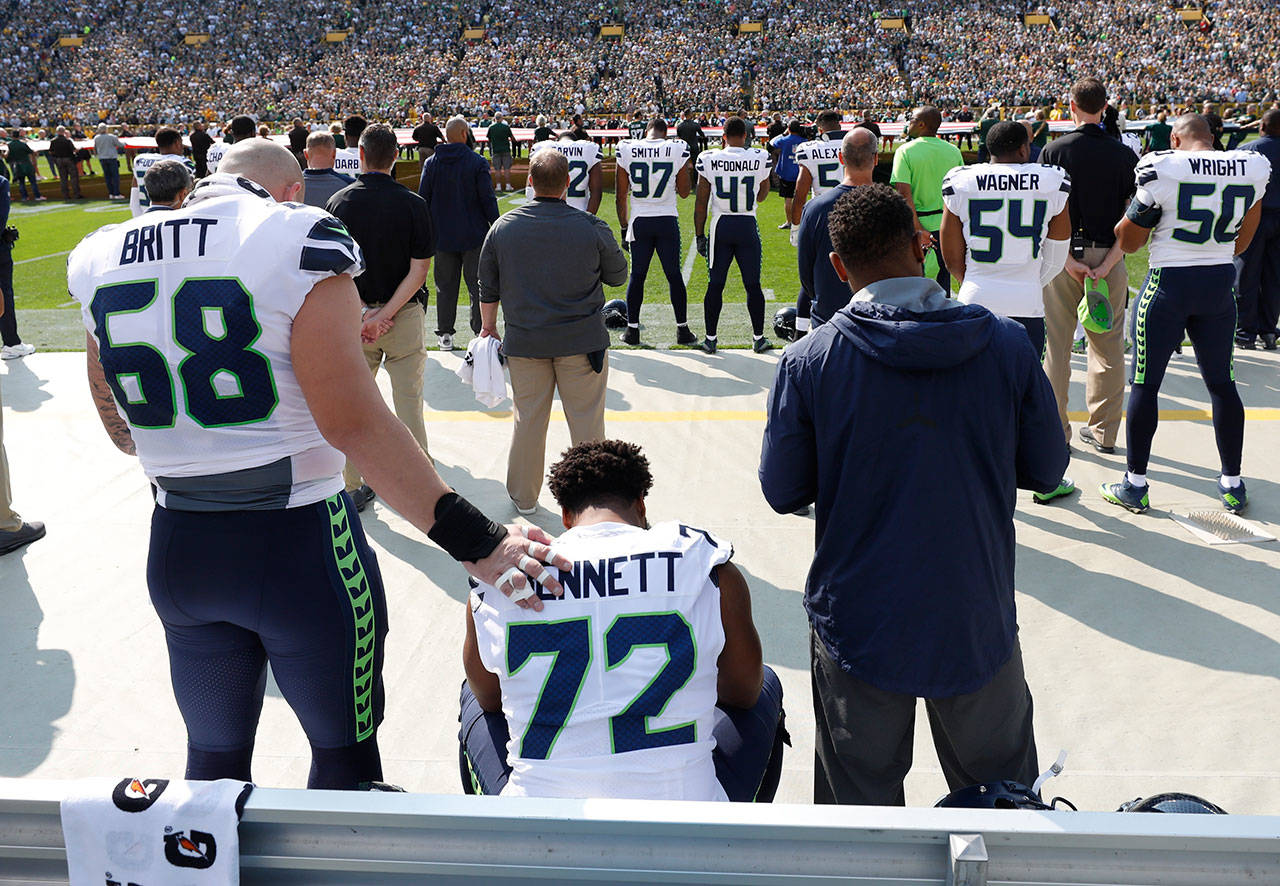 Former Seahawk Michael Bennett remains seated on the bench during the national anthem with teammate Justin Britt by his side before a game against Green Bay last season in Green Bay, Wis. (AP Photo/Jeffrey Phelps)