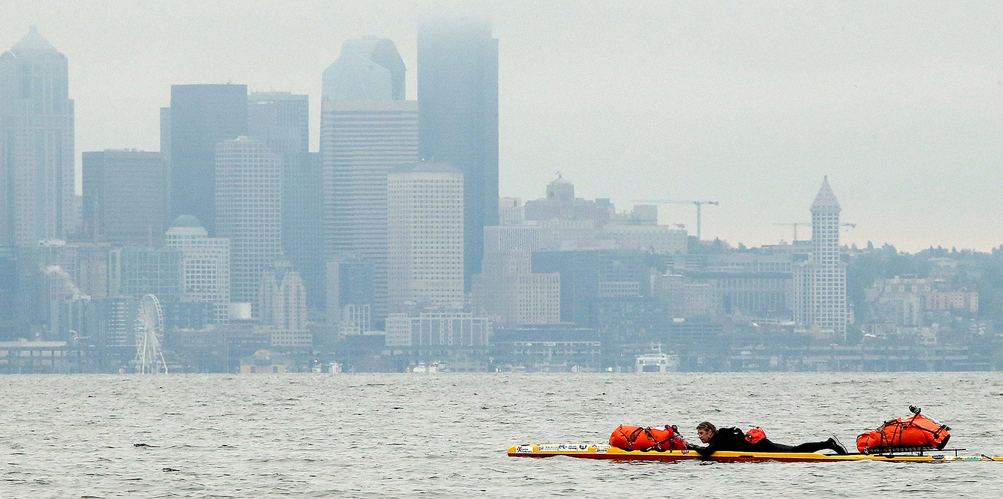 The Seattle skyline looms as Steve Rhoades paddles along the shore of Bainbridge Island. Rhoades will be paddling to Ketchikan, Alaska, this summer. (Meegan M. Reid/Kitsap Sun via AP)