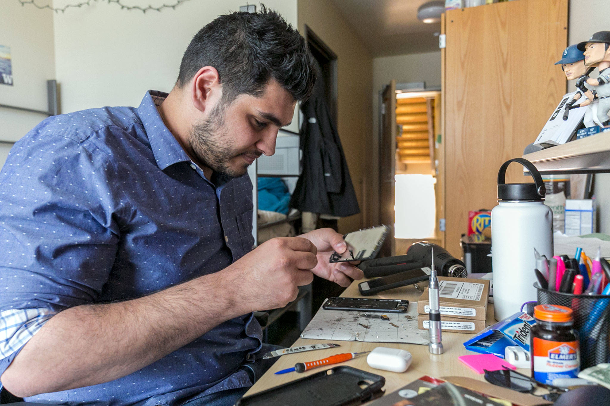 Amir Sultan repairs a phone in a dorm room at the University of Washington in Seattle. (Kevin Clark / The Herald)