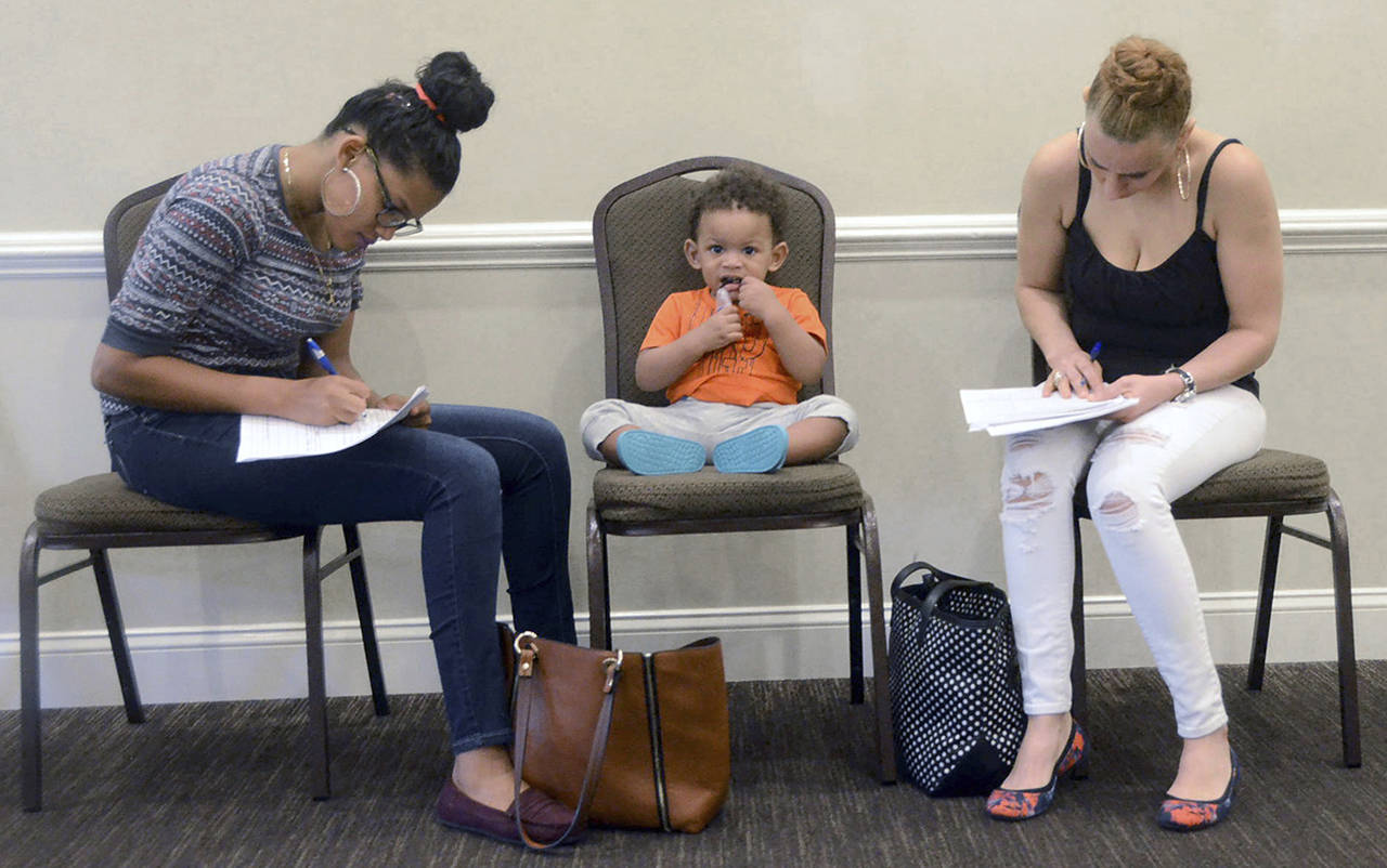 In this May 15 photo, Joan Herrera (center) sits and waits as his mother, Andrea Batista Garcia (left), and Marlene Gonzales (right) fill out job applications while attending the Great Northeast 2018 Job Fair at Capriottis in McAdoo, near Hazleton, Pennsylvania. (Ellen F. OConnell/Hazelton Standard-Speaker via AP, File)