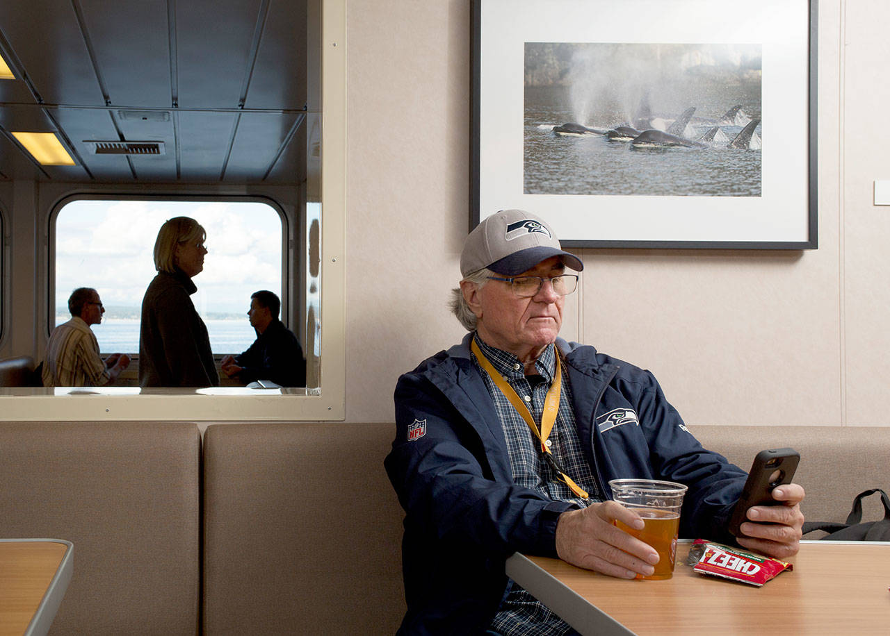 Tom French, of Freeland, looks at his cell phone while enjoying a Diamond Knot IPA during his commute home via the ferry Tokitae on Oct. 13, 2017. (Andy Bronson / The Herald)