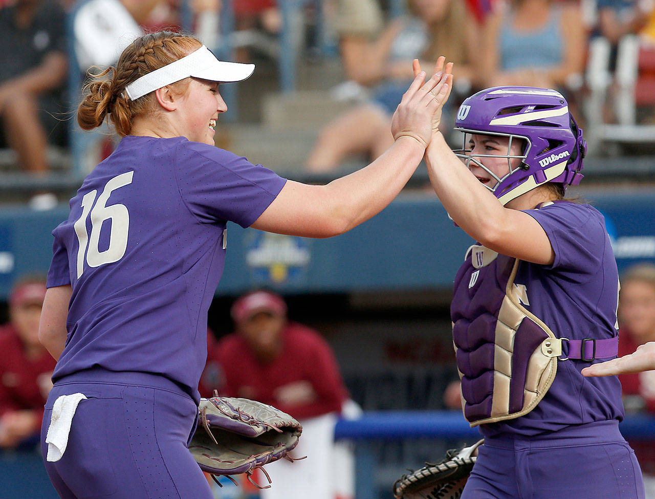 Washington’s Gabbie Plain (16) and former Meadowdale High School standout Emma Helm (right) exchange high-fives after the top of the third inning of Game 1 of the NCAA Women’s College World Series final Monday in Oklahoma City. Florida State beat UW 1-0. (AP Photo/Sue Ogrocki)
