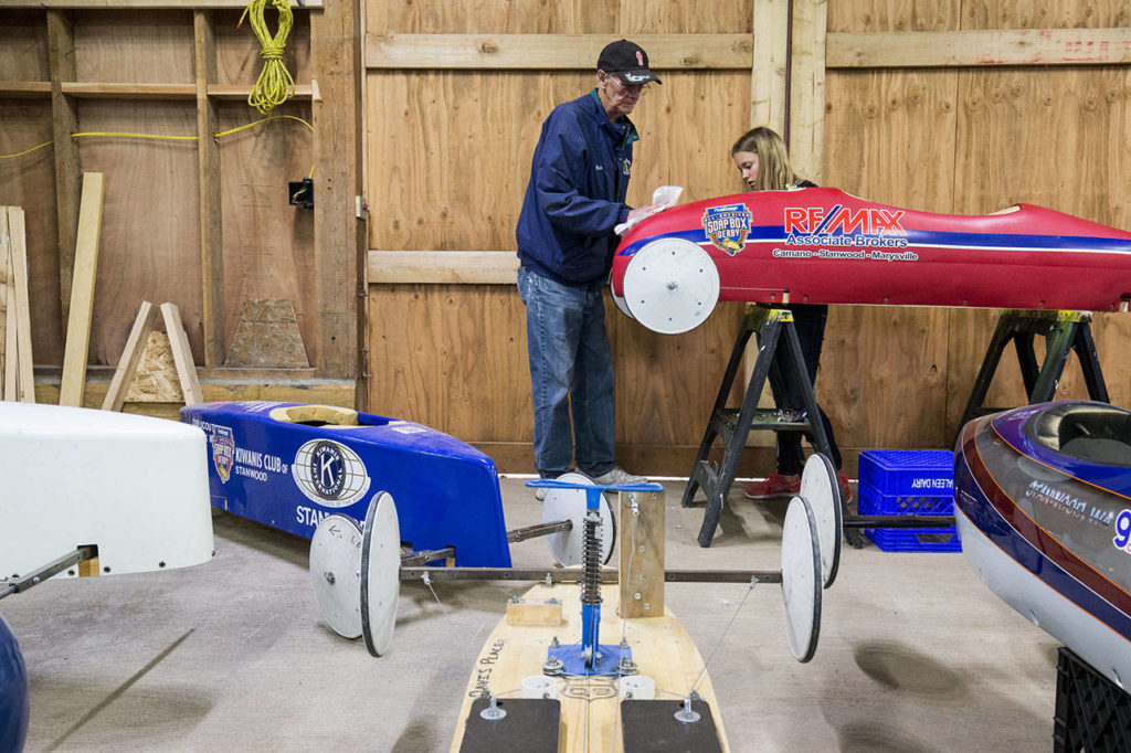 As her grandfather, Rich McCalib, wipes down the car, Alexie Crabtree removes a decal from her soap box car. (Andy Bronson / The Herald)
