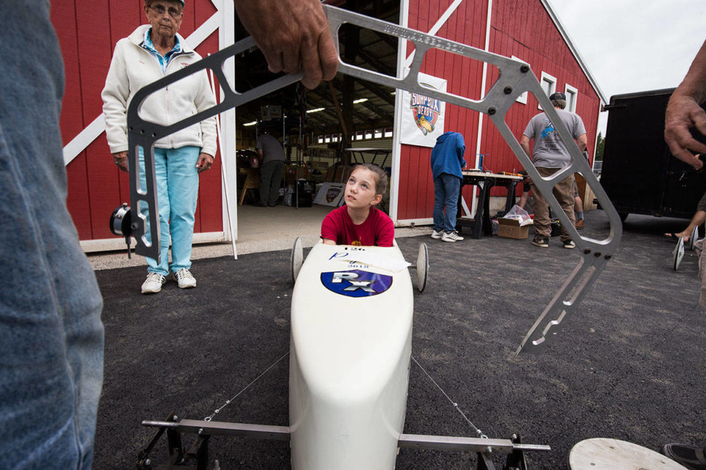 Peyton Calkins listens as adults talk about the bend in a rod that keeps the wheels straight under pressure from the driver’s weight in a soap box derby car. (Andy Bronson / The Herald)
